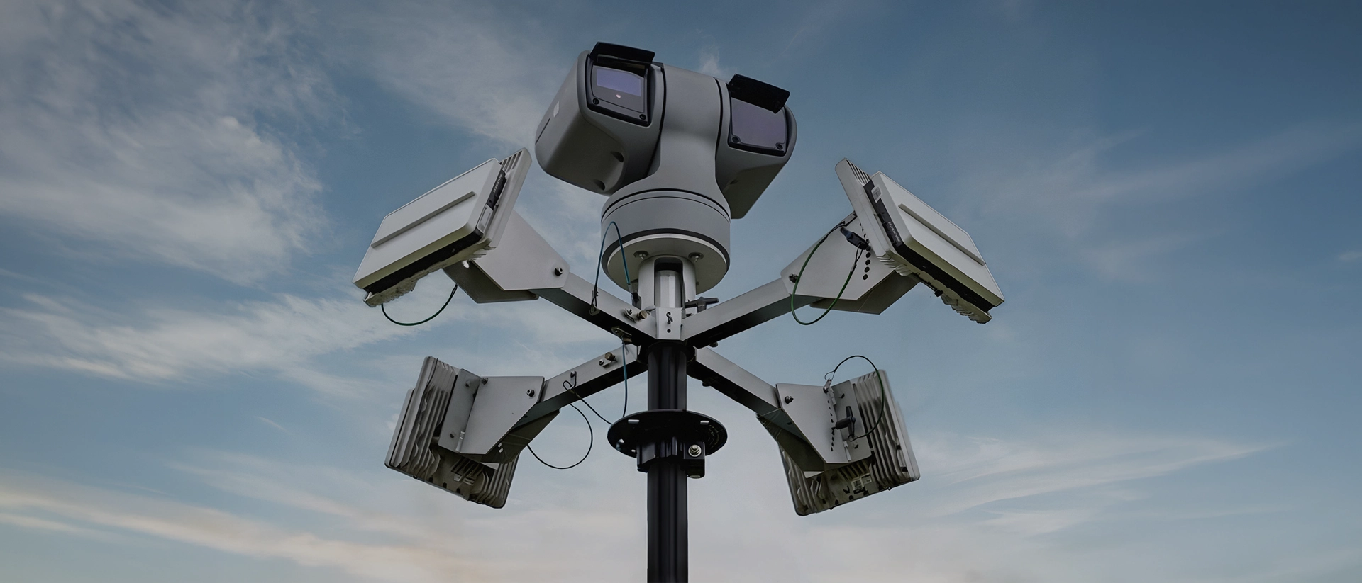 Multi-directional security camera system with sensors mounted on a pole against a cloudy sky.