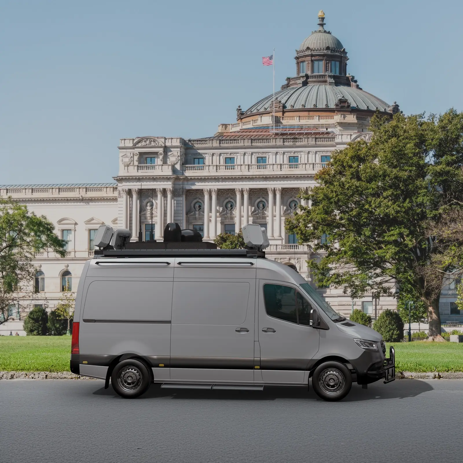 Gray radar-equipped van parked on street with historic domed building and US flag in background.