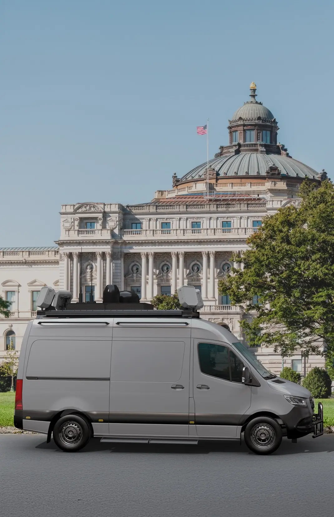 Gray surveillance van parked on street with historic building and U.S. flag in the background.