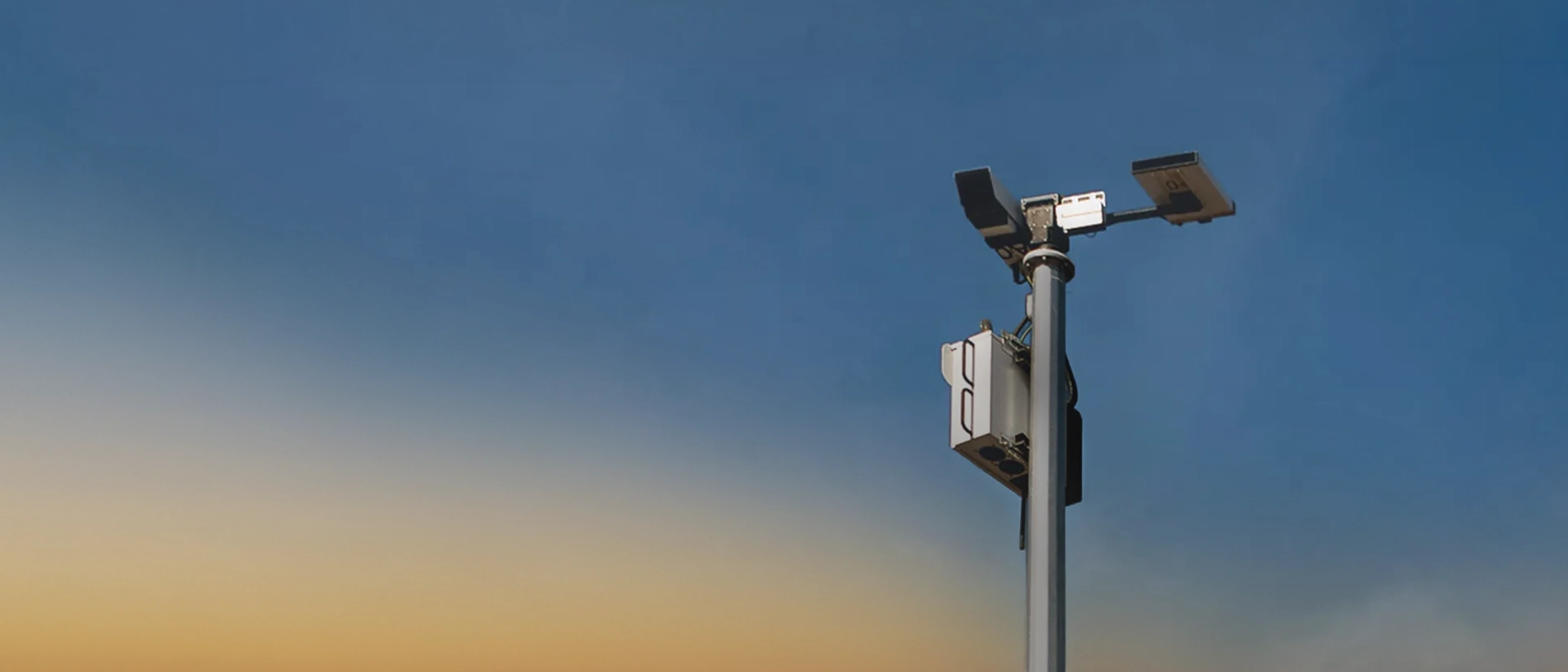 Security camera mounted on a tall pole against a blue and orange sunset sky.