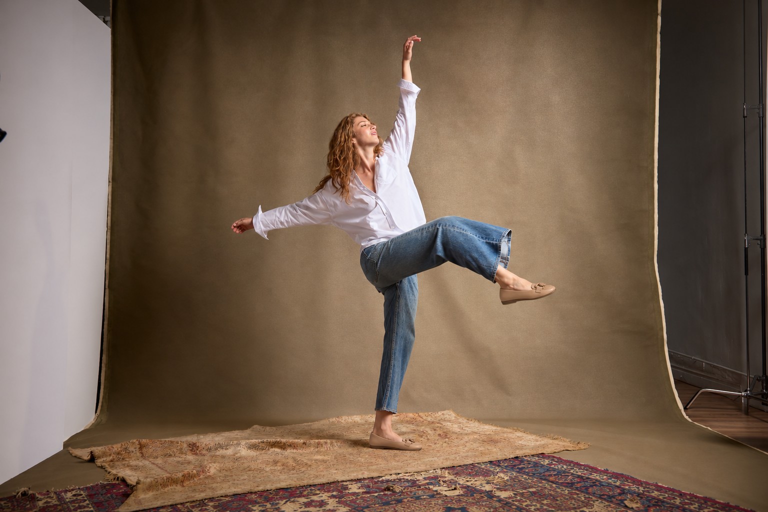 Woman in a joyful movement pose wearing beige flats in a warm-toned studio