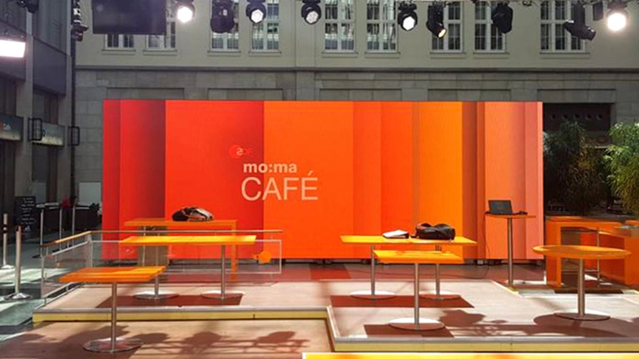 Ein TV-Studio mit orangefarbenen Tischen und Stühlen vor einer großen Cold-LED-Wand.