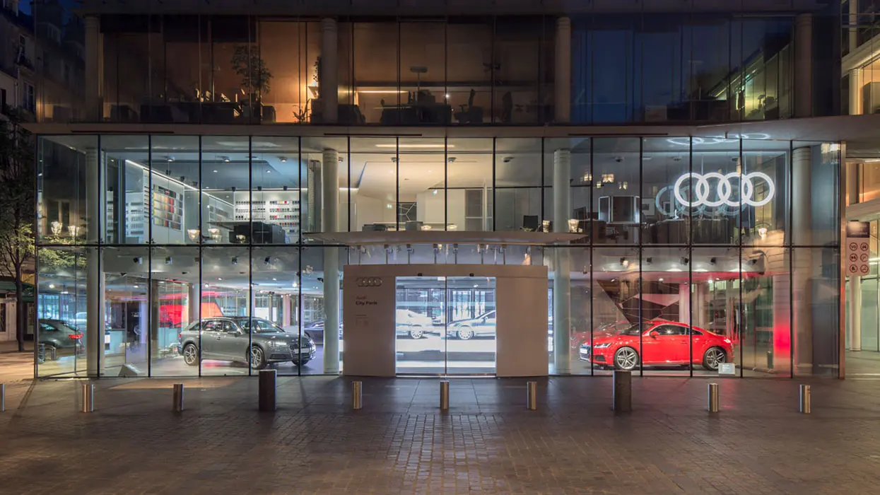 Glazed facade of an Audi City showroom with vehicles and digital display surfaces.