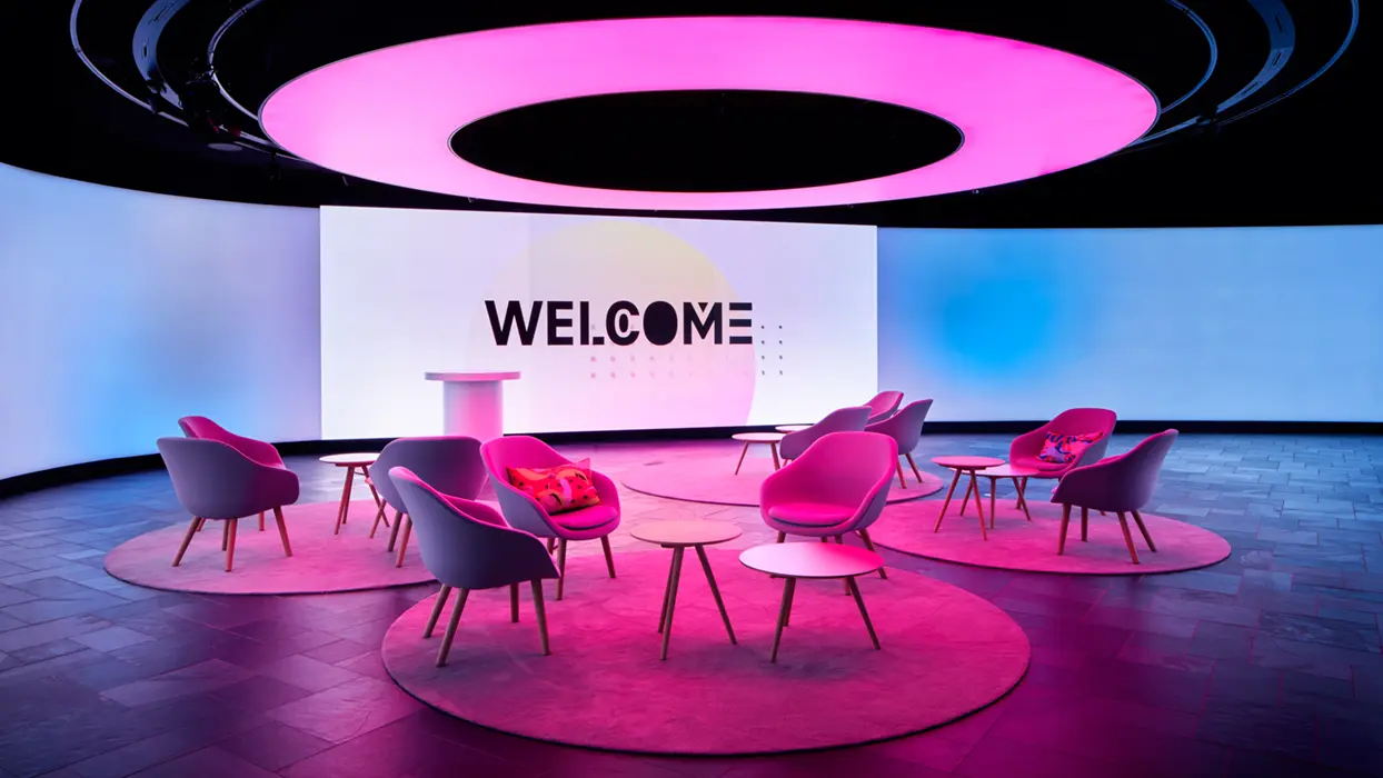Event space in the Telekom T-Gallery with three large display surfaces, seating areas and ring-shaped ceiling lighting.