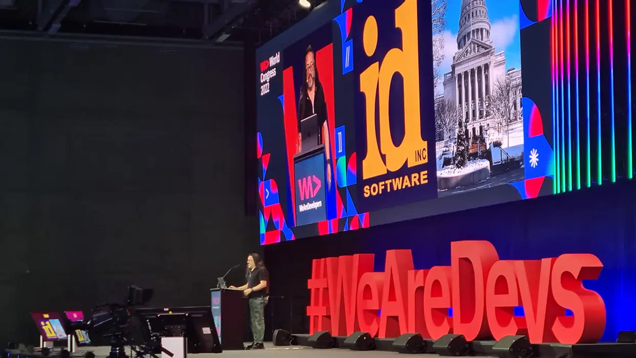 Speaker in front of a large LED screen and red WeAreDevs lettering on a conference stage.