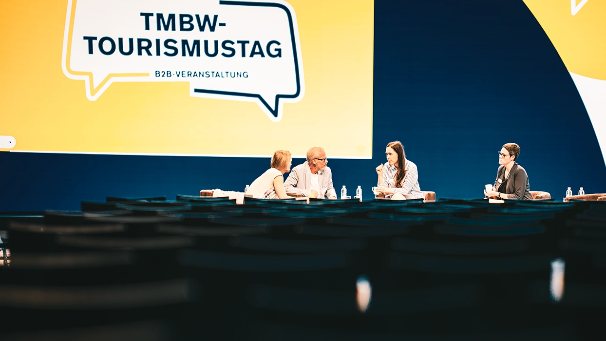Panel discussion in front of a large LED stage display showing the title TMBW-Tourismustag.