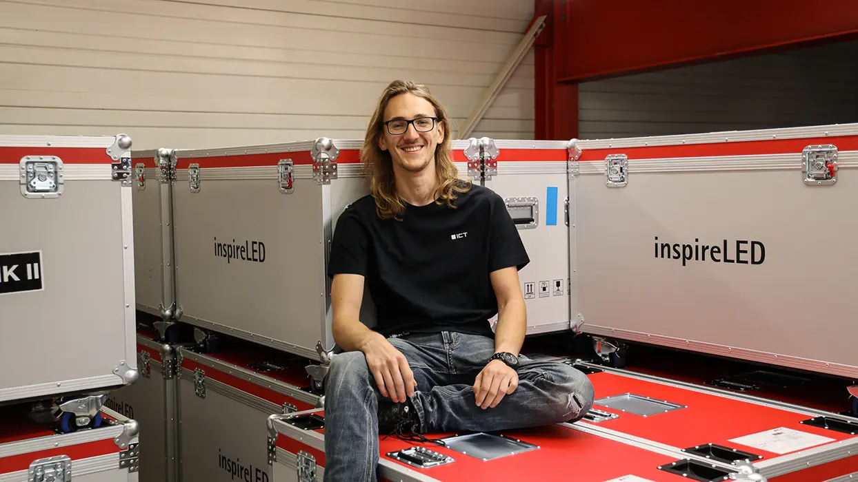 Person wearing an ICT shirt between stacked transport cases for LED equipment.