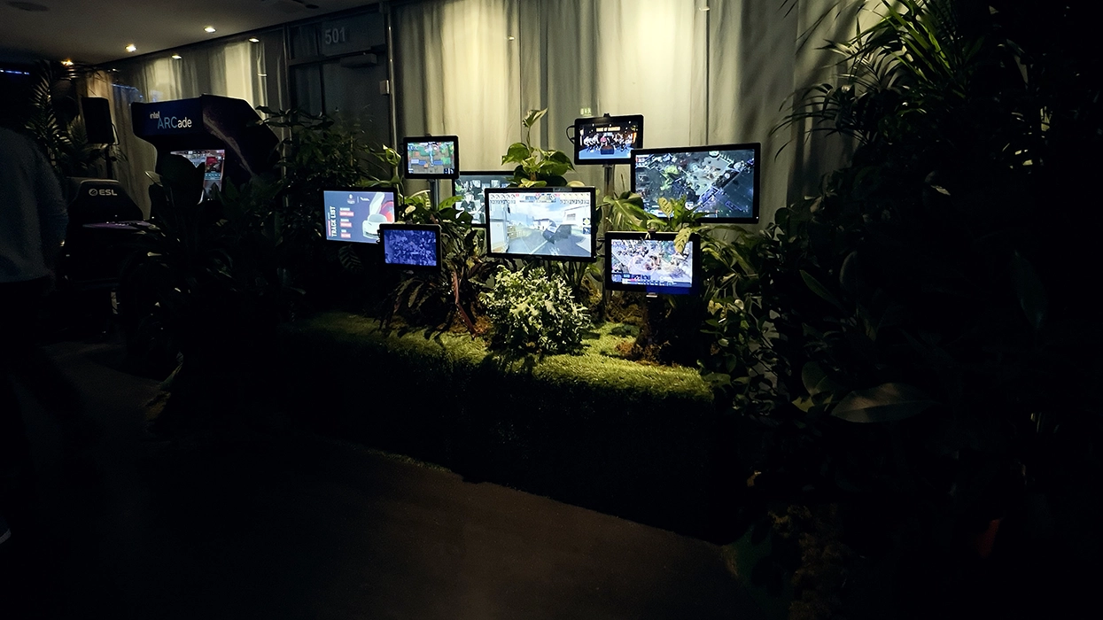 A group of people standing in front of a display of monitors and plants.