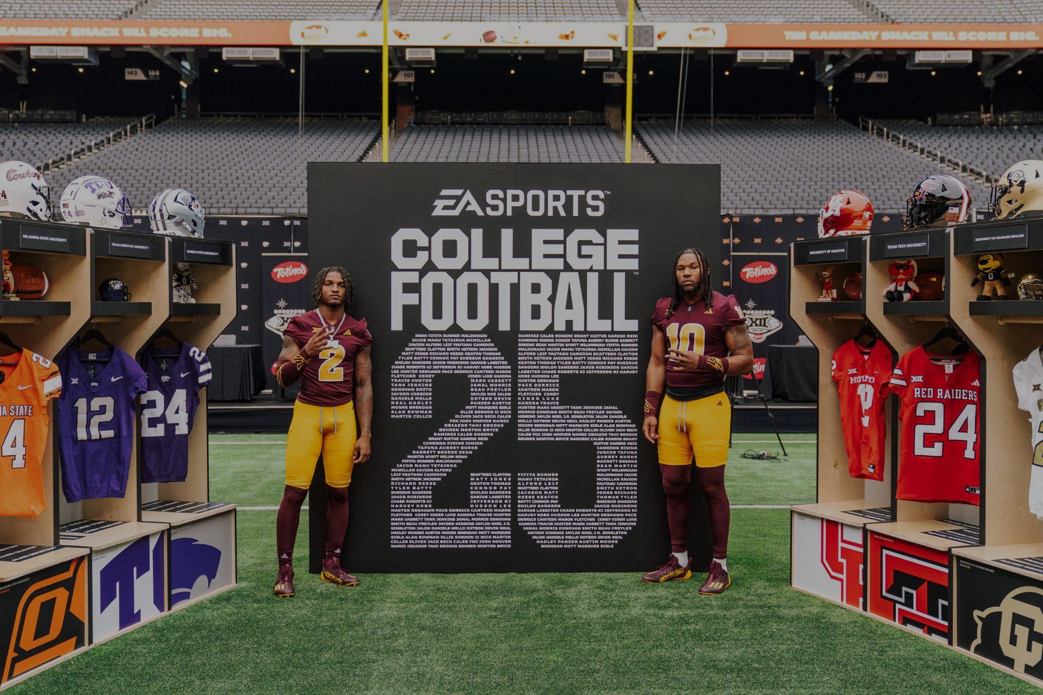Two college players pose in front of a College Football 25 wall of player names between team lockers
