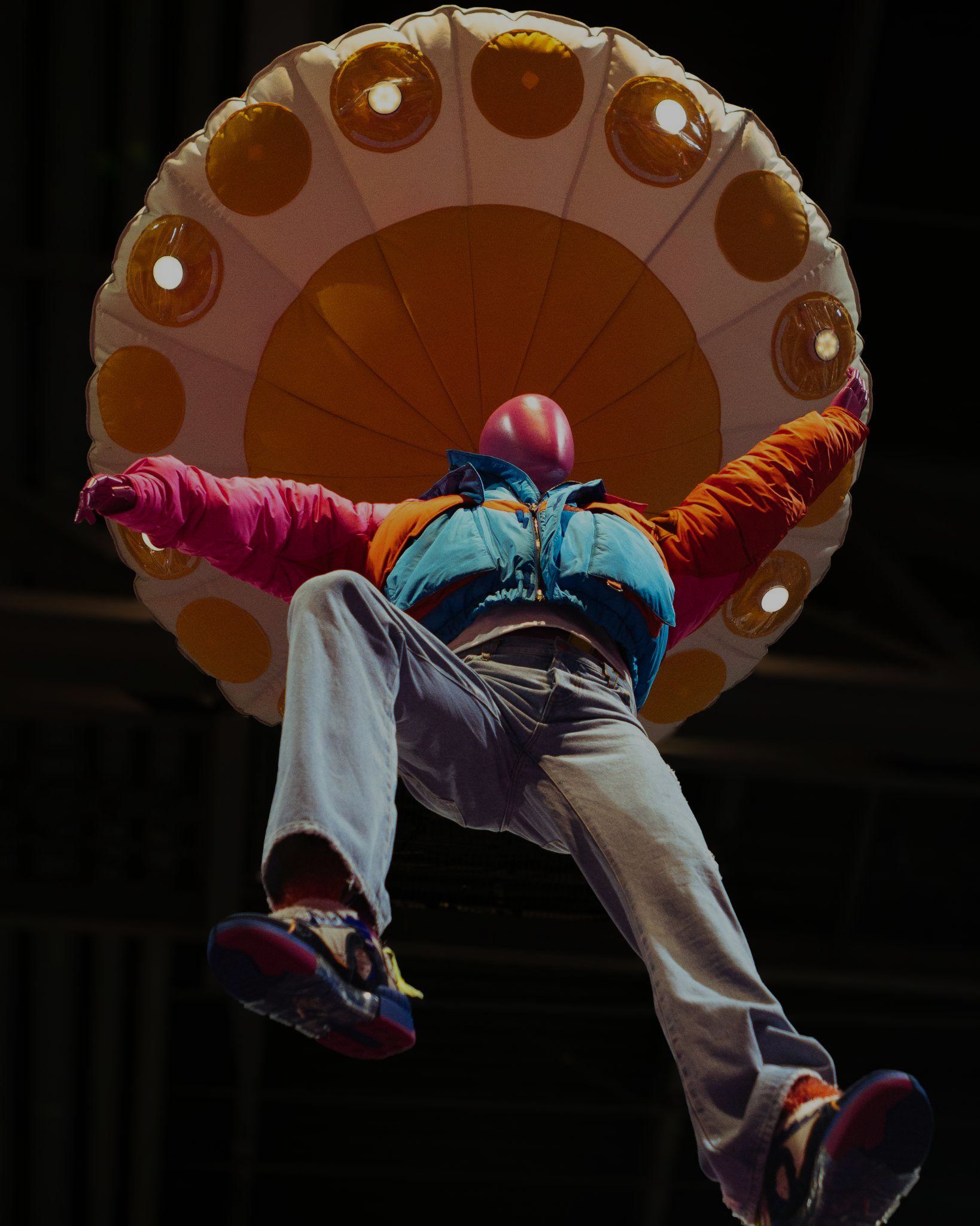Figure in a puffer jacket suspended beneath an inflatable UFO at the Members of the Rage install