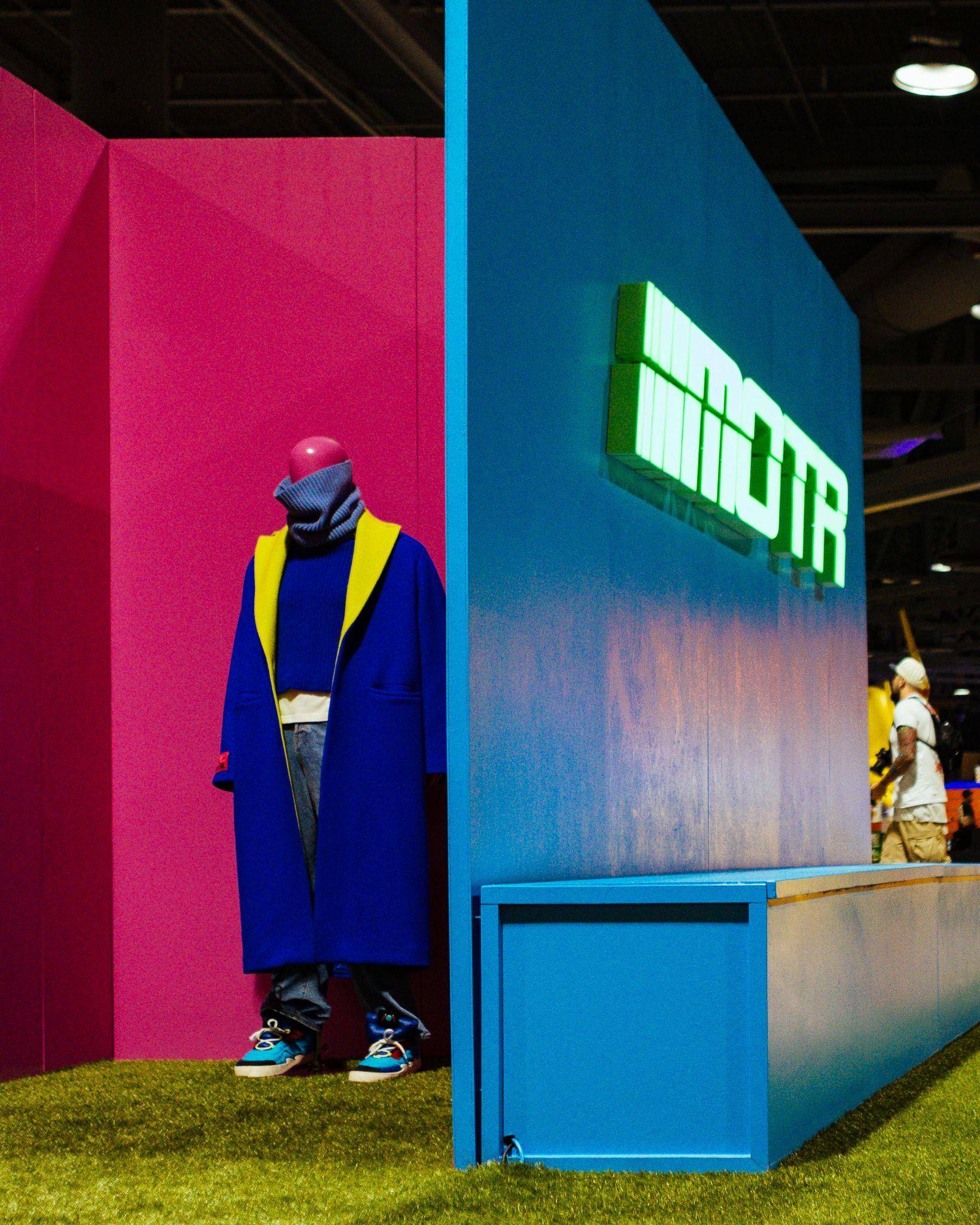 Members of the Rage booth with a blue wall, neon MOTR sign and a mannequin on turf