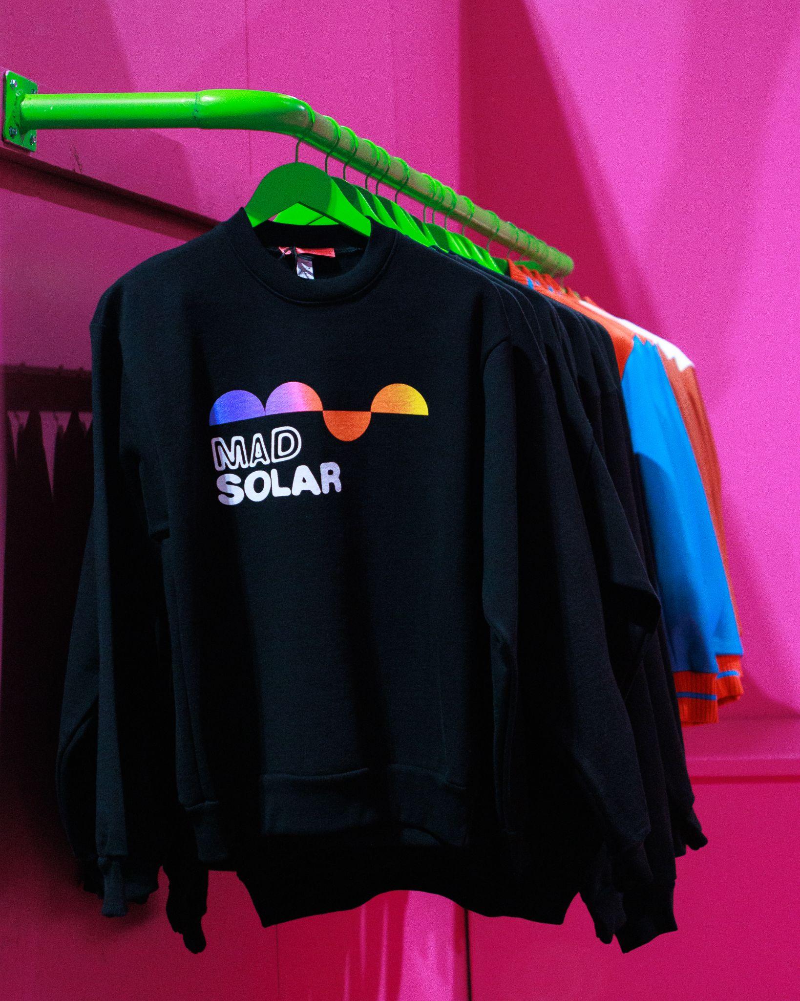 Mad Solar sweatshirt on a green rack against pink walls