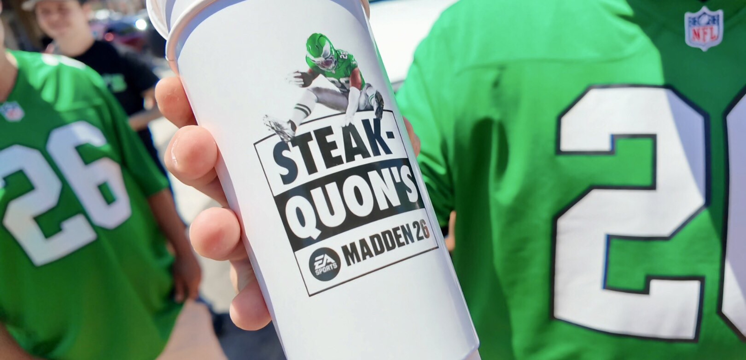 Fan holds a Steakquon's Madden 26 cup in front of an Eagles jersey