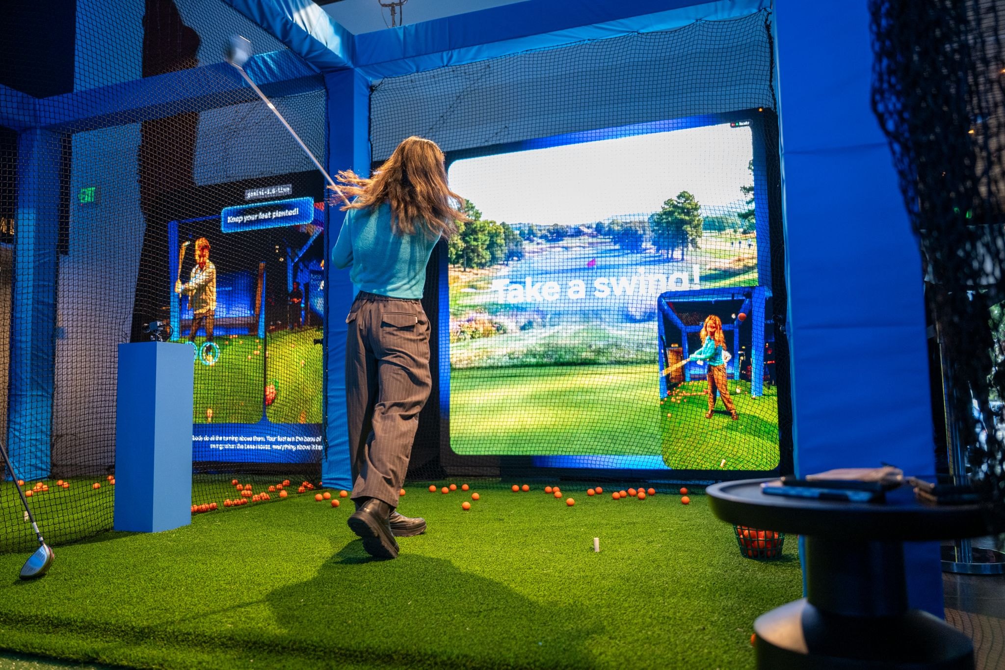 A guest swings at the Audio Range golf sim while Gemini Live coaches her form on screen