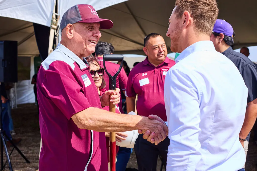 A district official in a maroon polo shakes hands with an Upward Communities representative under a tent at the Wildflower Lockhart groundbreaking ceremony