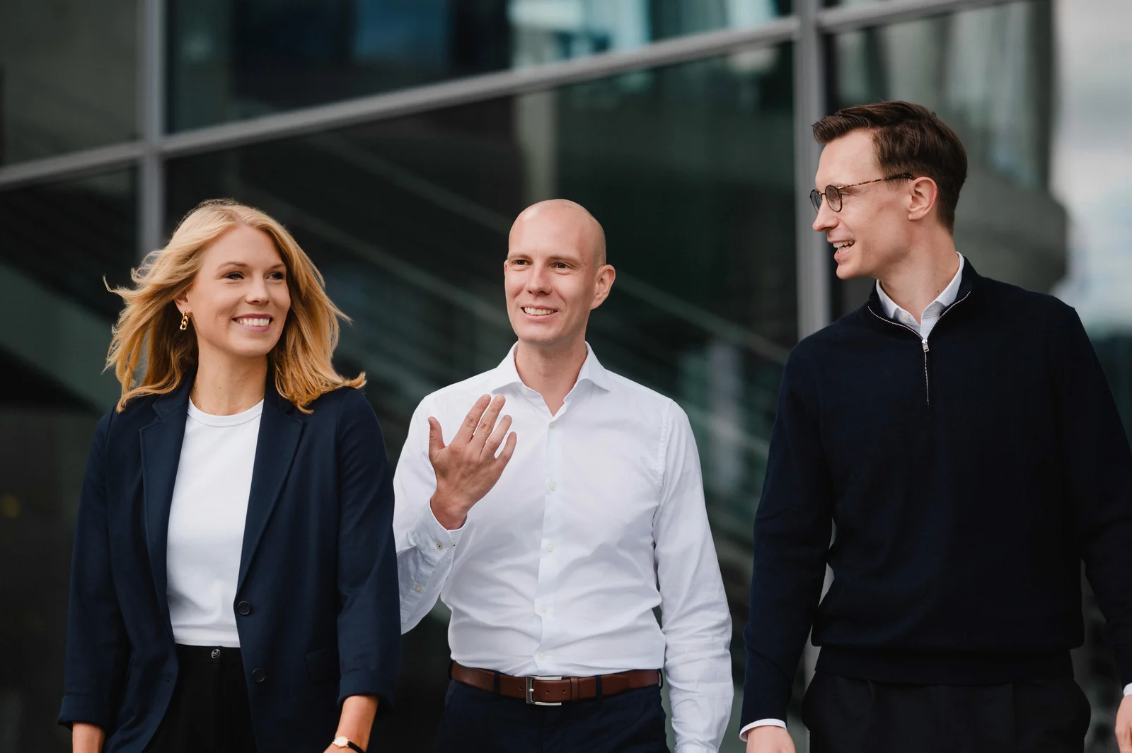 Drei Personen im Business-Outfit gehen vor einer Glasfassade