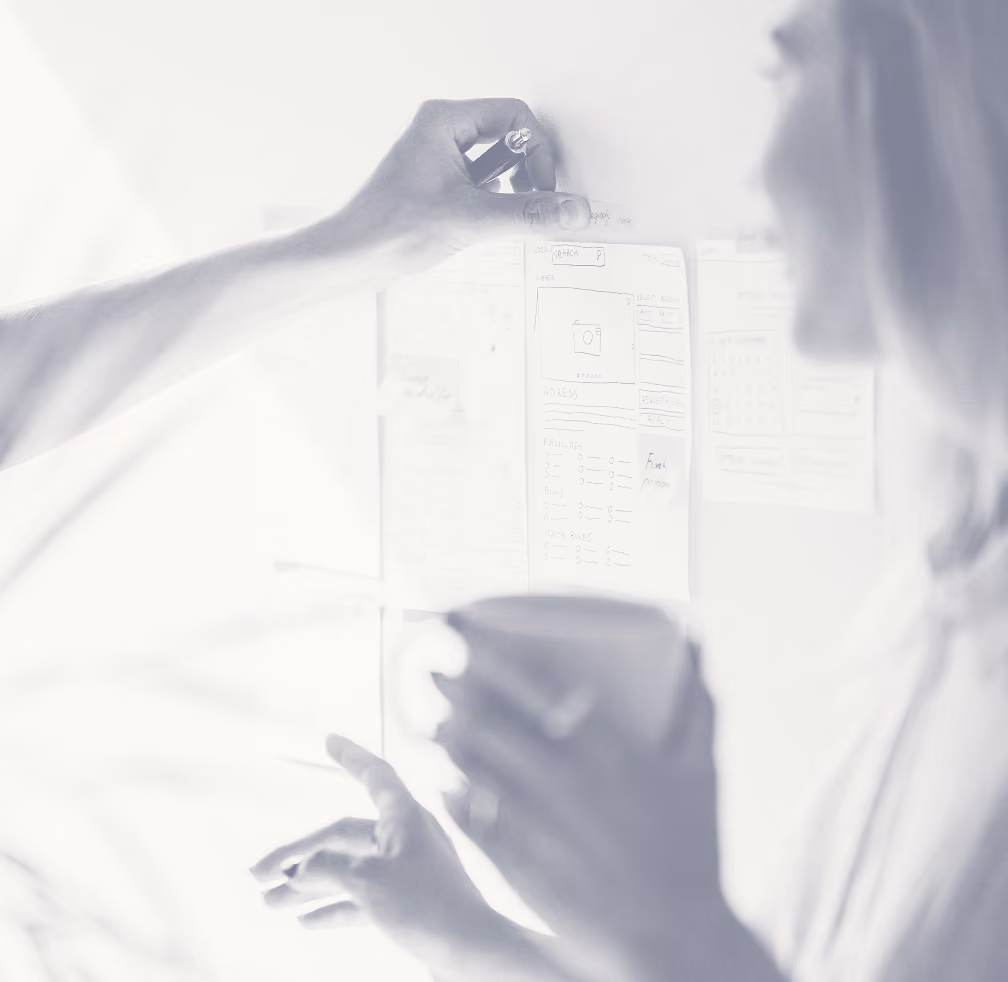Two people collaborating in front of a whiteboard with diagrams and notes, one holding a marker and the other with a cup.