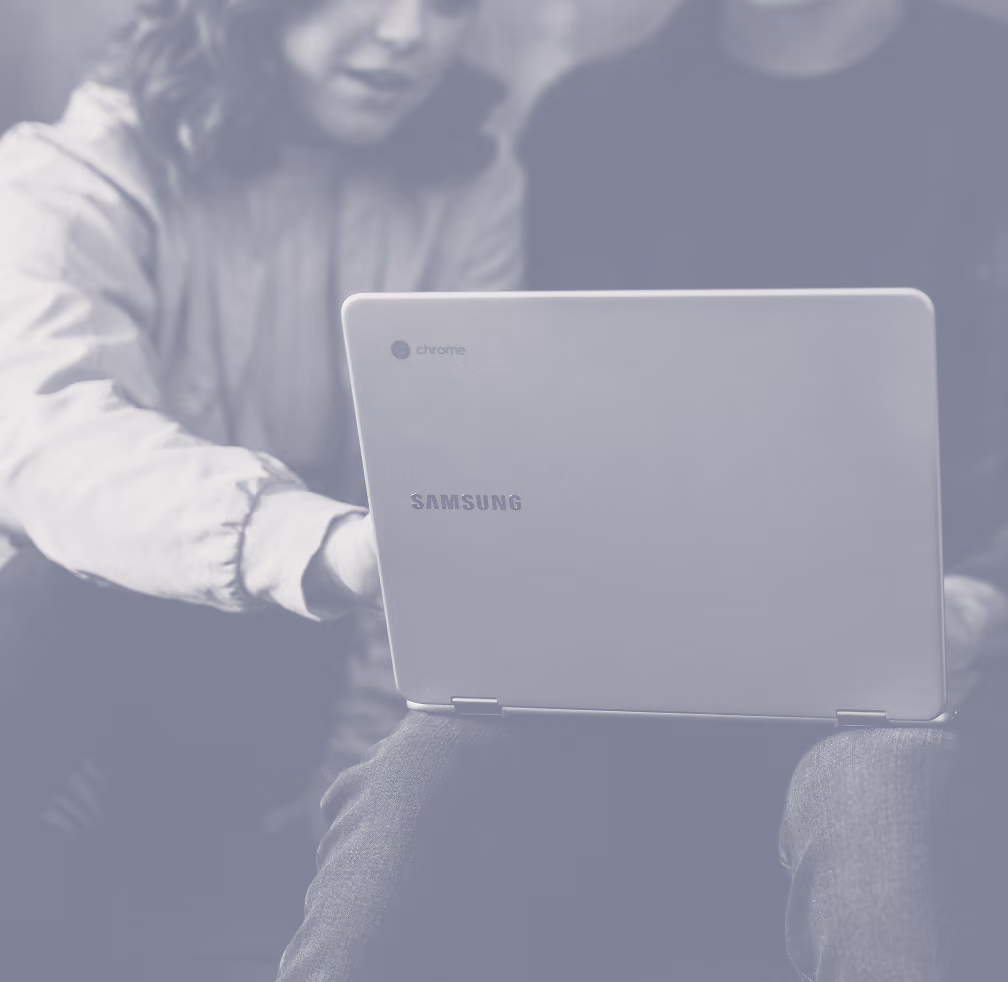 Two people closely looking at the screen of a Samsung Chromebook laptop, with one person pointing at it.