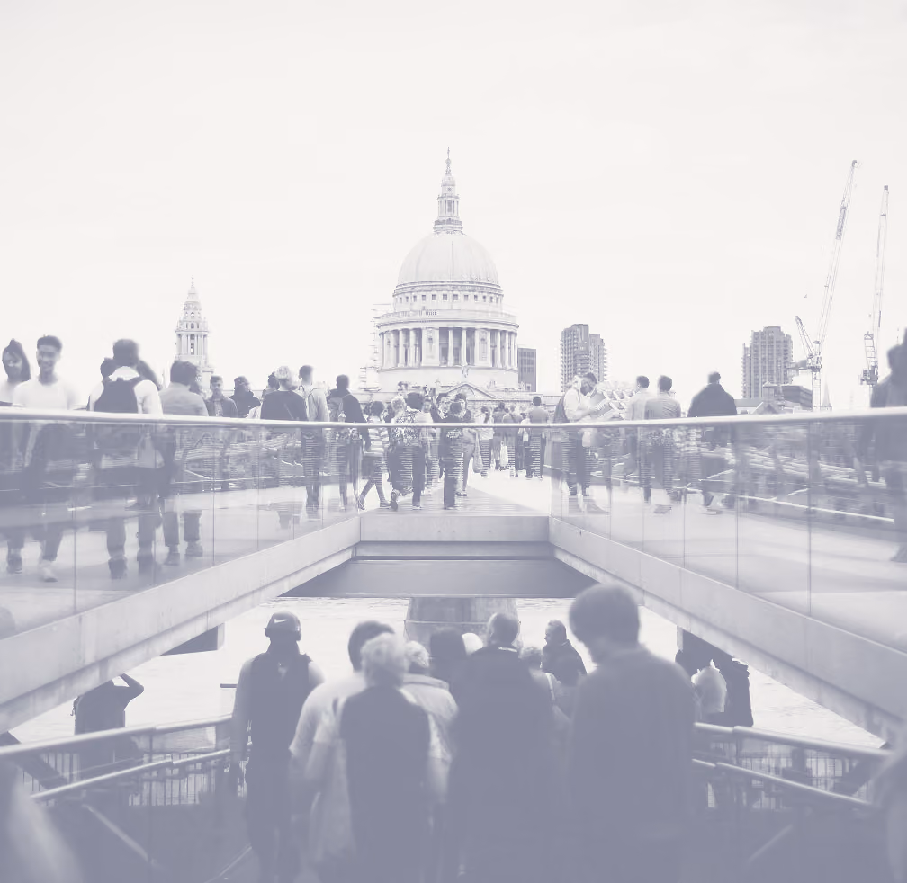 Crowds of people walking along Millennium Bridge in London with St Paul's Cathedral prominent in the background under an overcast sky.