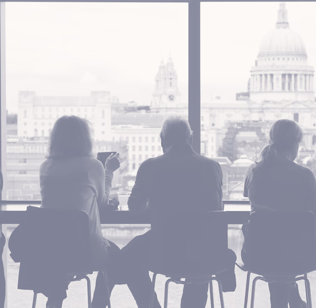 Silhouettes of three people sitting on chairs facing a large window overlooking a cityscape with historic buildings, including a prominent domed structure.