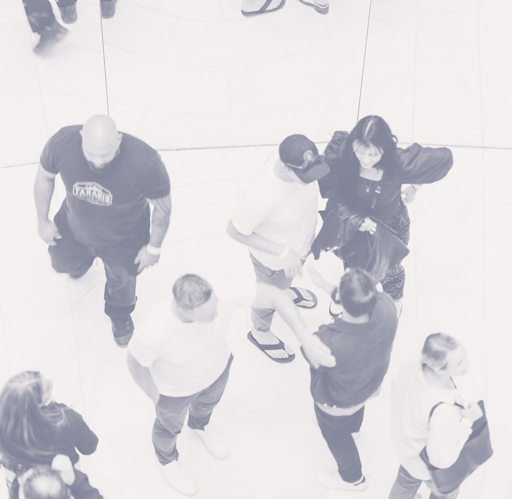 Overhead view of eight people standing and walking in a bright, reflective space creating mirrored reflections of their legs and feet on the floor.