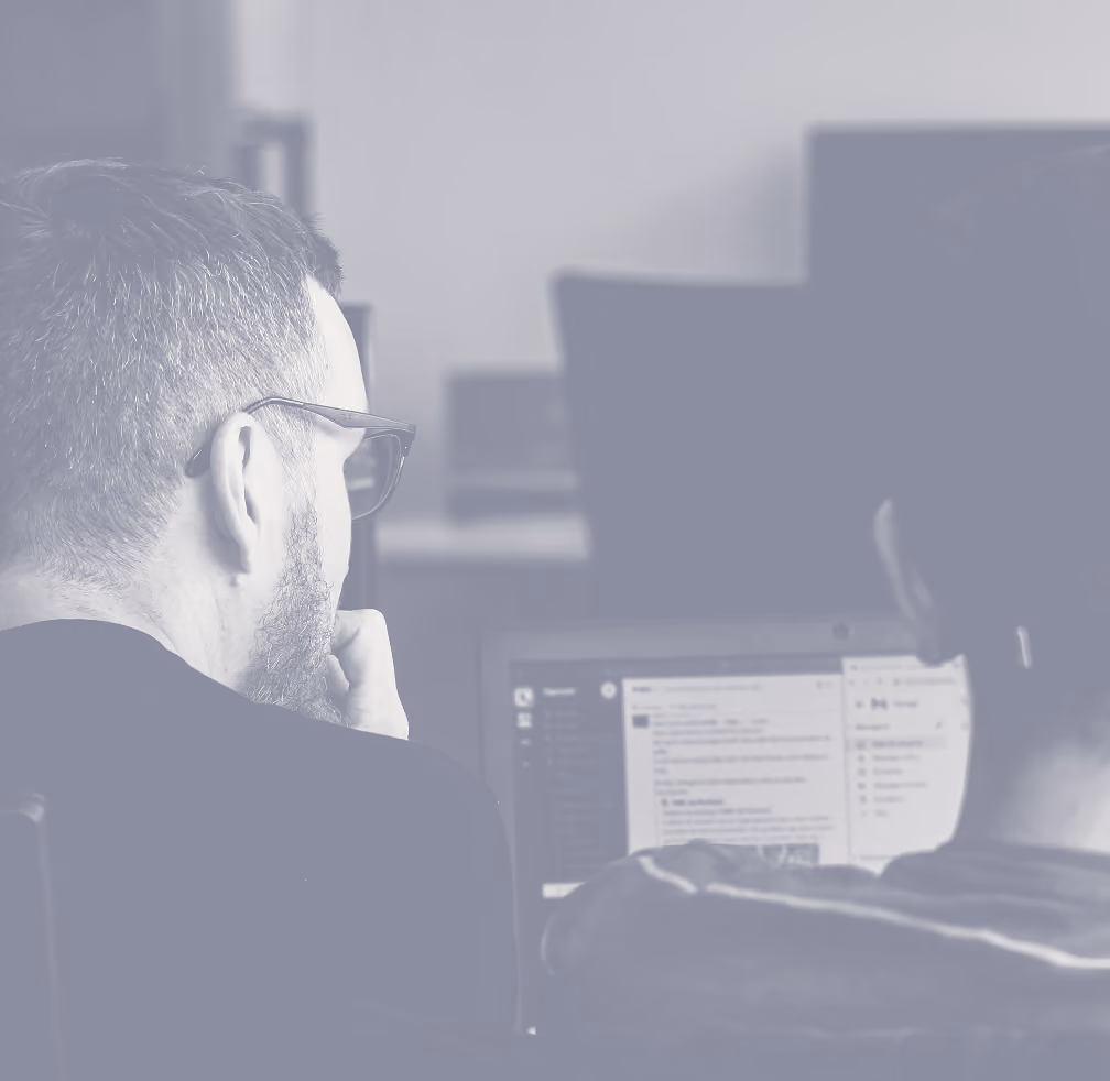 Two people viewed from behind working together on a laptop displaying a message or chat interface in a workspace.