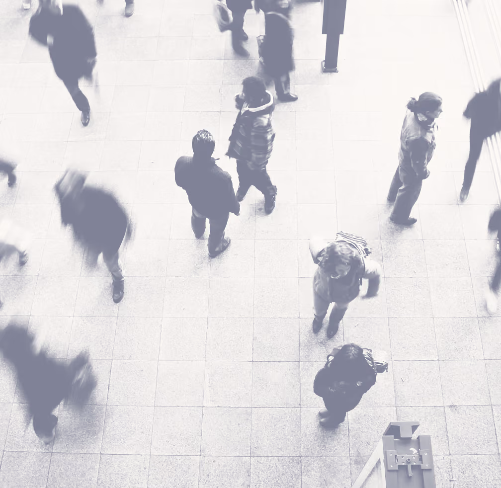 Overhead view of people walking and standing on a large tiled floor in a public indoor space, with some figures blurred by motion.