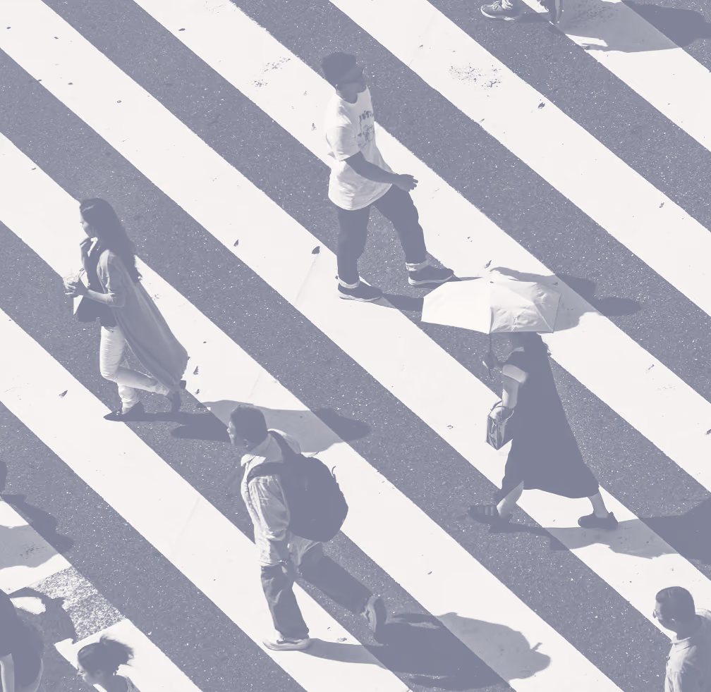 Overhead view of people crossing a street on a zebra crossing, including a person holding an umbrella and others walking in different directions.