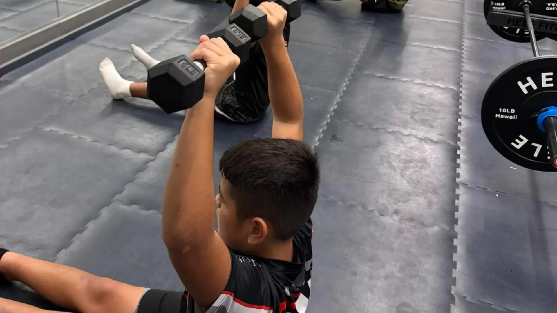 Young athlete performing a dumbbell strength exercise during a training session at ATHLTX Sports Performance in Waipahu, HI.
