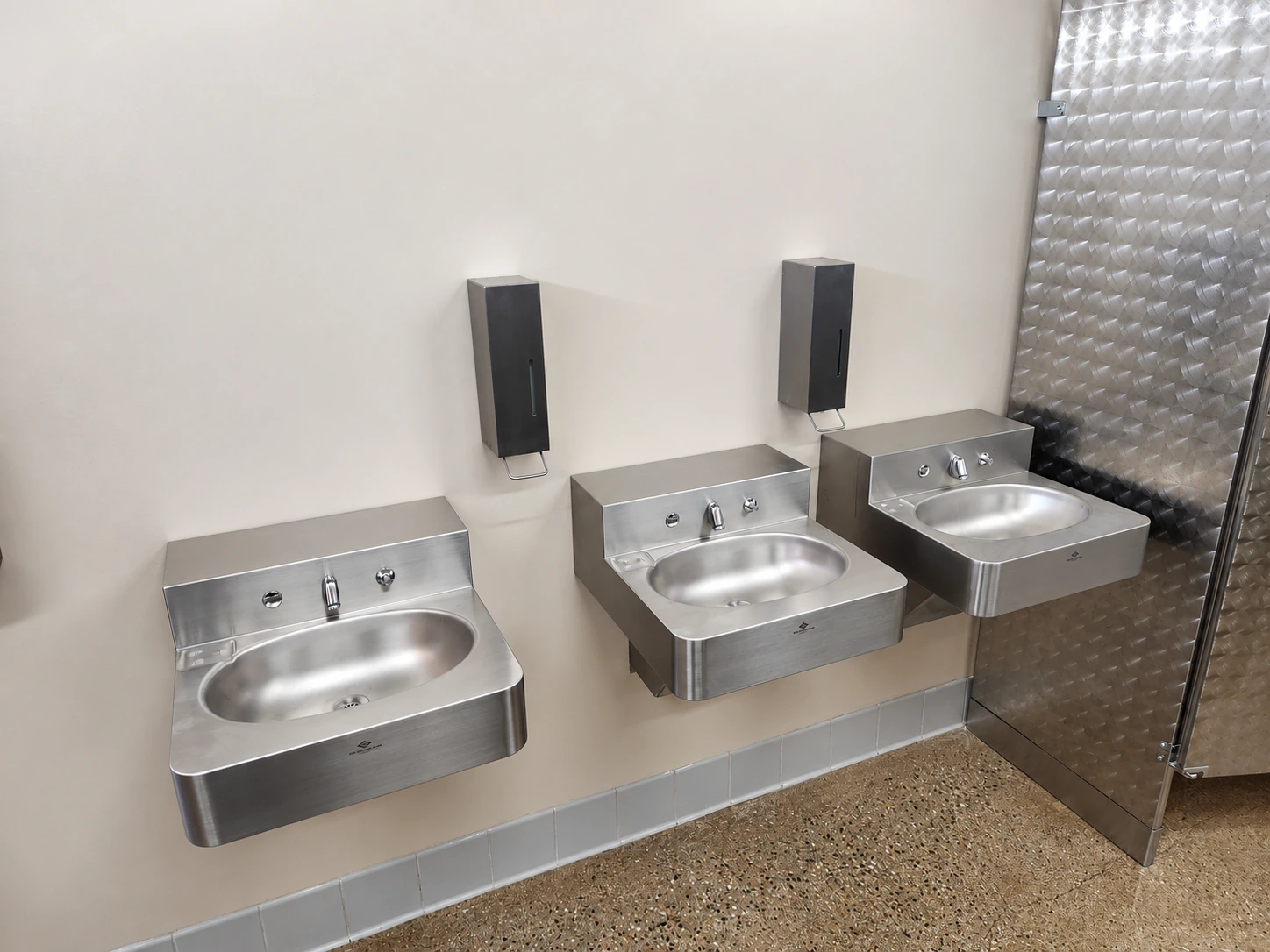 Three stainless steel wash stations and wall-mounted soap dispensers in the completed Northwest Park restroom.