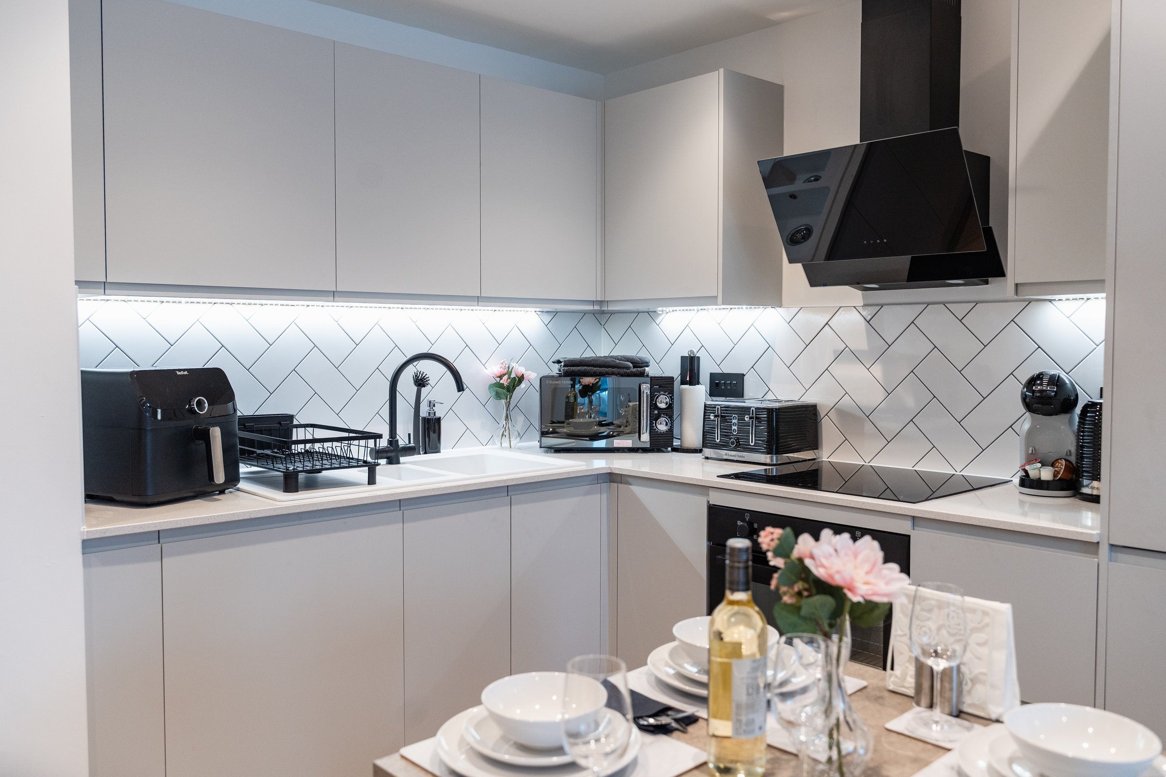 Kitchen with white units, a black cooker hood and a laid dining table in front