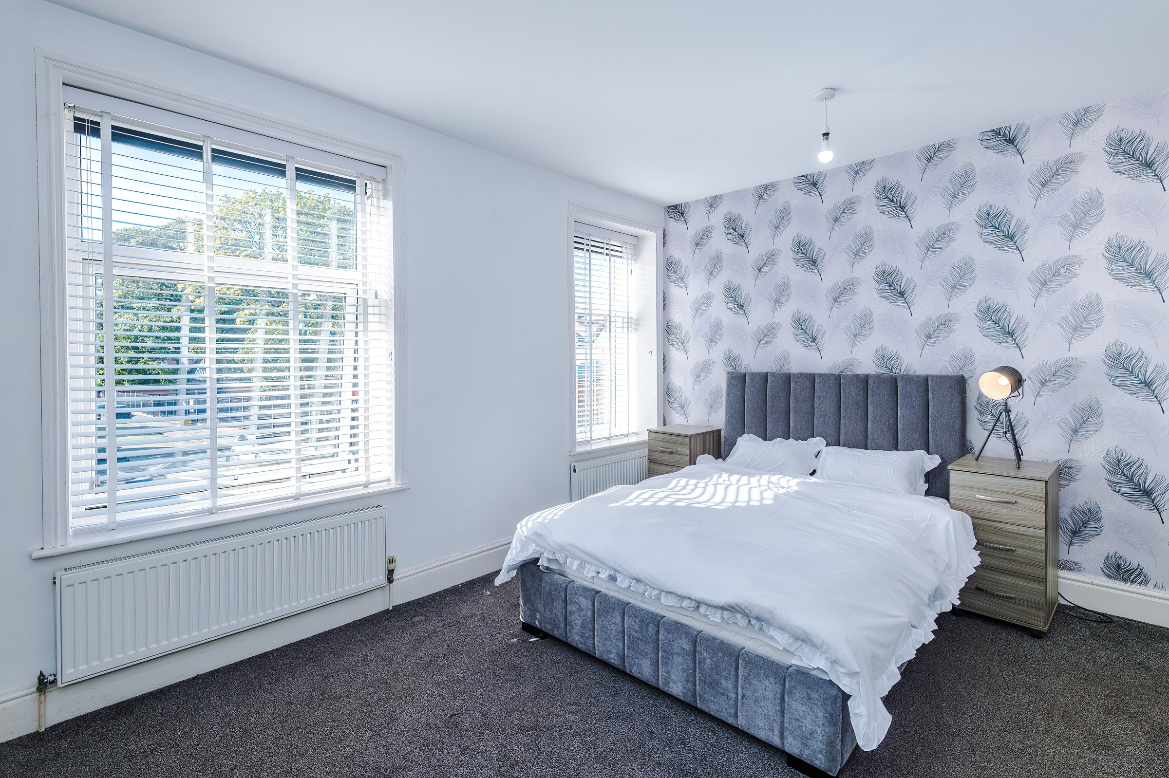 Bedroom with a double bed, grey headboard and feature wallpaper beside the window