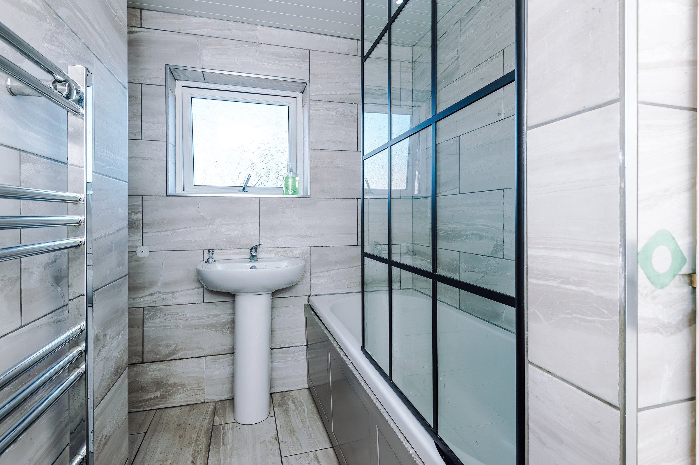 Bathroom with a basin, heated towel rail and a bath with a glass shower screen
