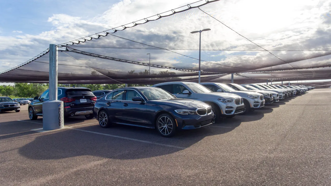 Row of BMW vehicles parked under Hail No protective netting in a dealership lot