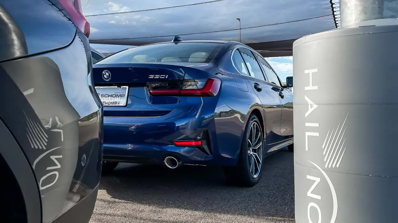 Close-up of a BMW 330i sedan parked under a Hail No canopy system in a dealership lot