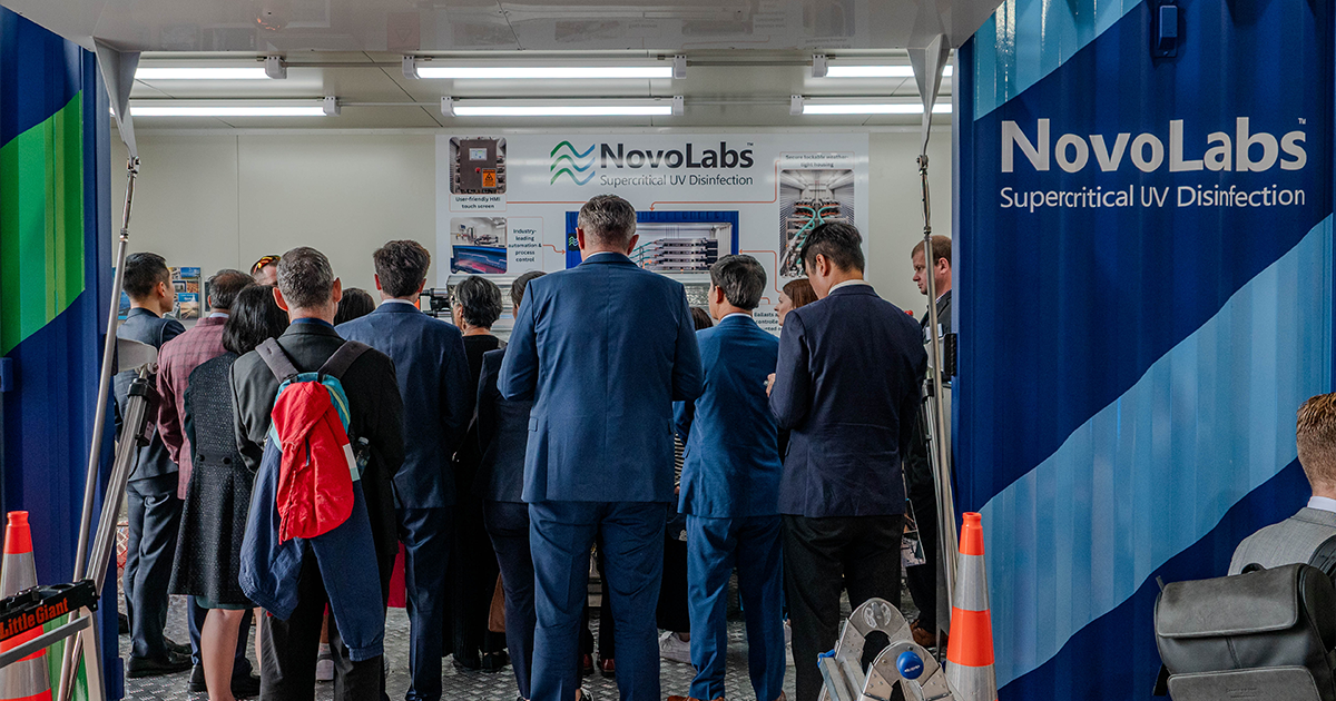 Group of people in suits viewing a NovoLabs Supercritical UV Disinfection display at an event.