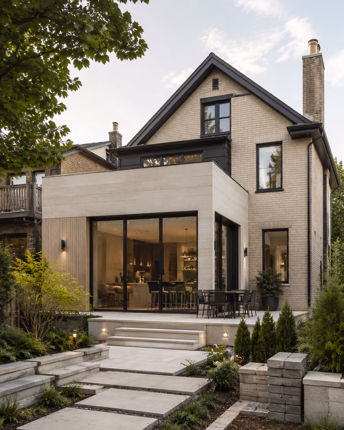 Modern house with beige brick exterior, large glass doors, patio, stairs, and landscaped garden.