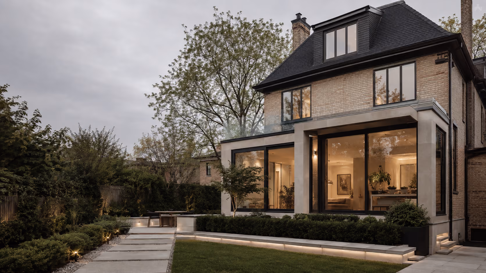 Modern brick house with large windows and a lit, landscaped garden patio at dusk.