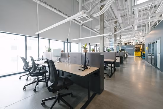Modern open space office with rows of desks and ergonomic chairs near large windows.