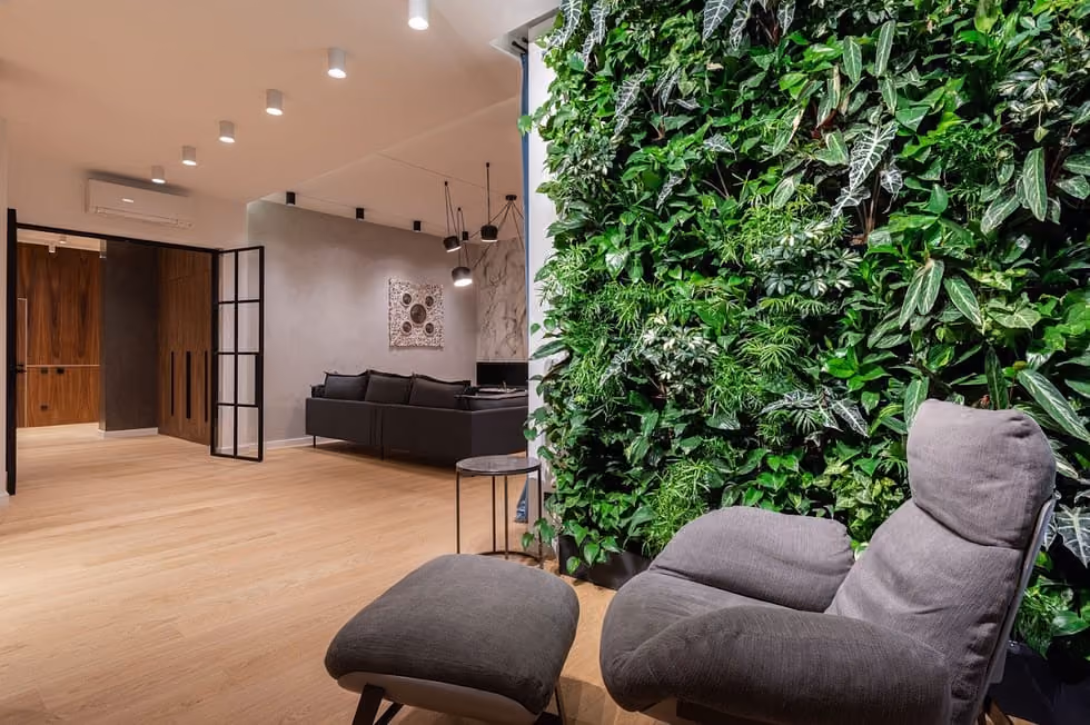 Modern interior with a green plant wall, gray lounge chair, ottoman, and a cozy seating area.
