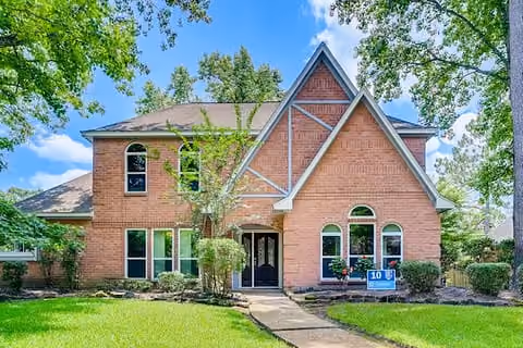 Two-story brick house with steep gable roof, arched windows, and a green lawn with trees.