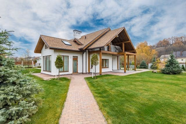 Modern house with pitched roof and a brick pathway surrounded by green lawn and trees.