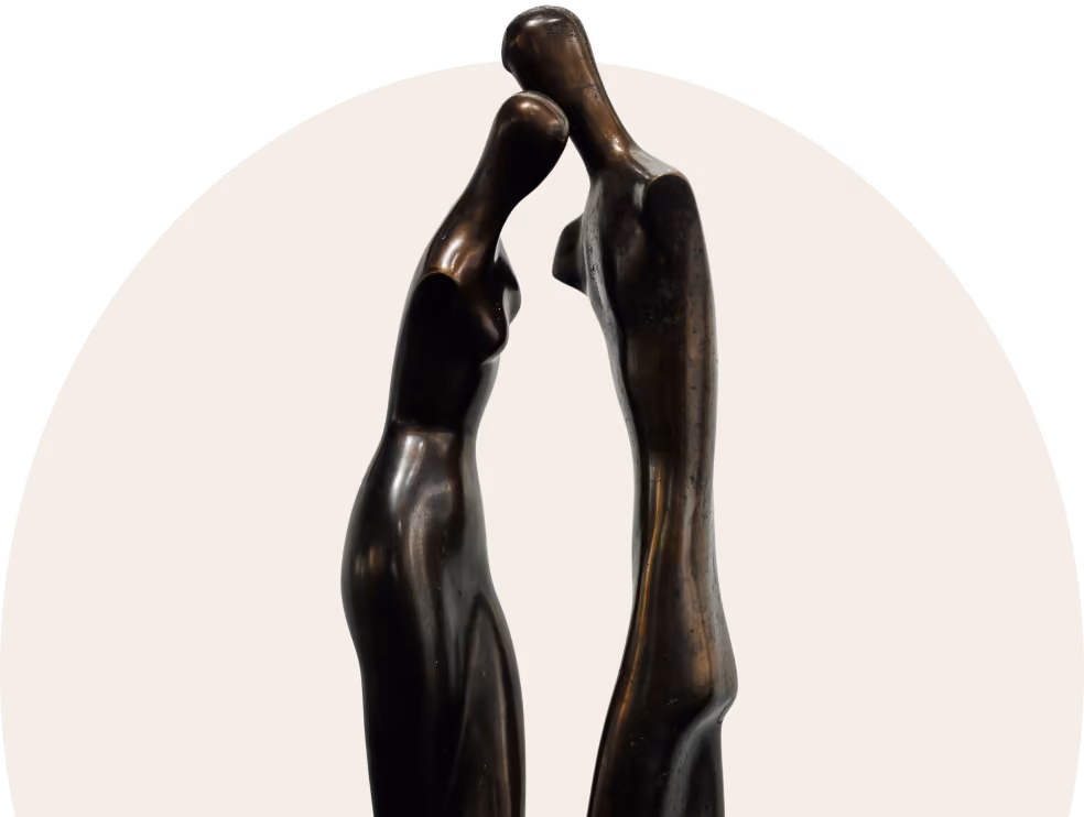 Abstract bronze sculpture of two elongated human figures leaning heads together.
