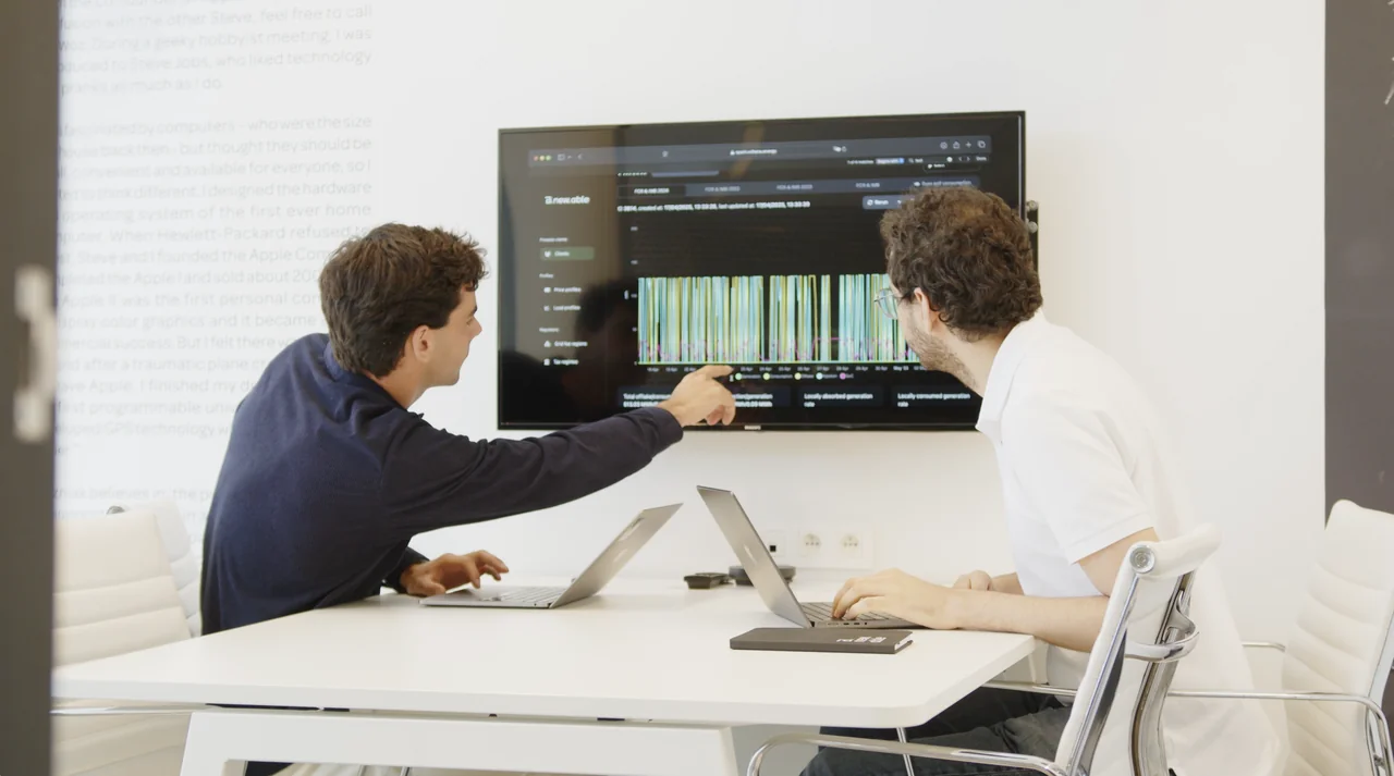 Two Bnewable colleagues in a meeting room reviewing energy generation and consumption charts in the Voltana dashboard on a wall-mounted screen.