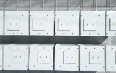 White battery modules stacked in racks inside an industrial hall, with the roof structure visible above