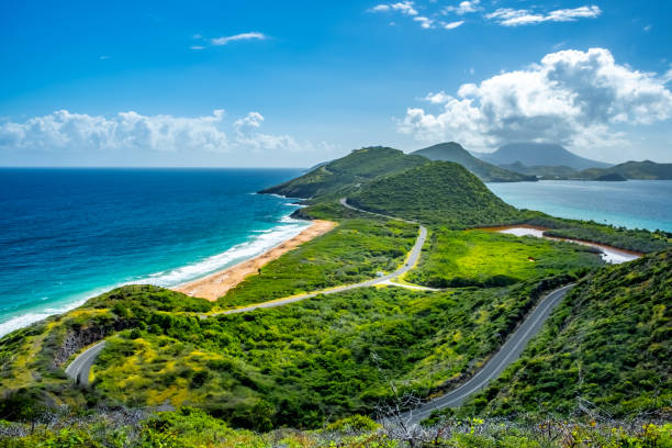 Coastal landscape with winding roads, green hills, blue ocean, and partly cloudy sky.