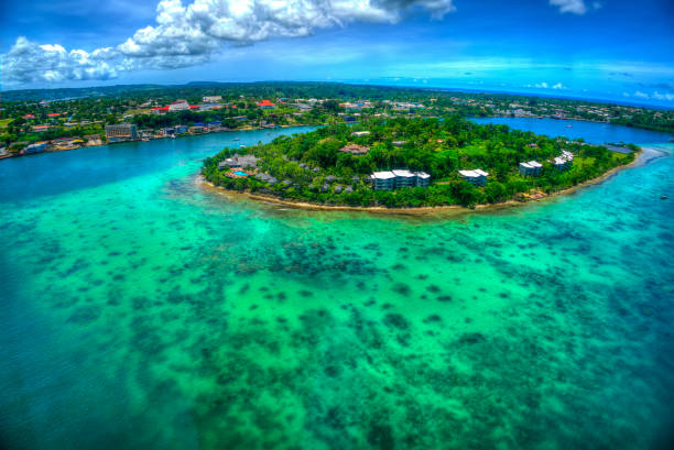 Aerial view of a lush green island surrounded by clear turquoise waters and buildings along the shore.