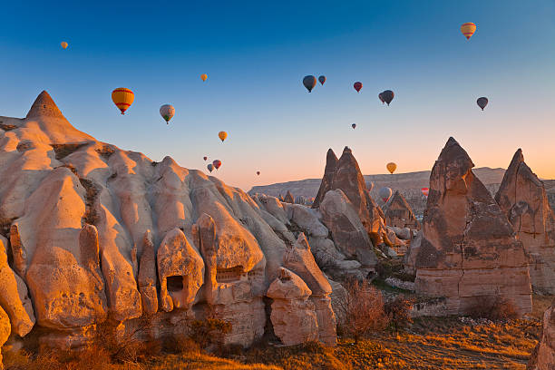 Hot air balloons flying over unique rock formations in a scenic sunset landscape.