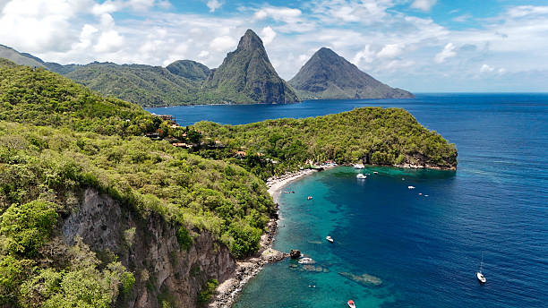 Aerial view of lush green coastline with clear blue water and two mountainous peaks in the background.