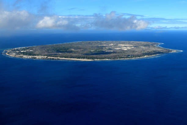 Aerial view of a flat island surrounded by deep blue ocean under a partly cloudy sky.